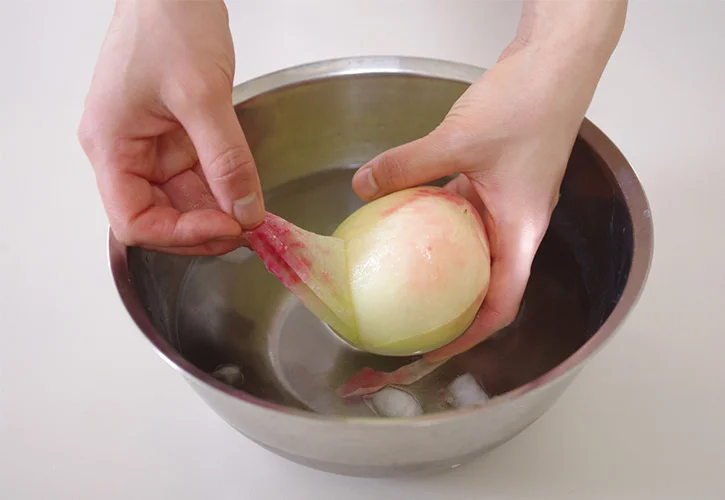 氷水に取り手で桃の皮をひっぱる